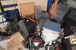 Eine überfüllte Garage voller verschiedener Gegenstände, darunter Fahrräder, Kisten, Werkzeuge und verstreute persönliche Besitztümer.