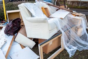 Ein Haufen ausrangierter Möbel und Holzreste aus einer Wohnungsräumung am Straßenrand, darunter ein weißer Sessel und ein zerlegter Holzschrank.