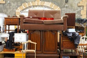 Eine Auswahl an Möbeln, darunter ein braunes Sofa auf einem Holzschrank, umgeben von verschiedenen anderen Antiquitäten im Dachboden.