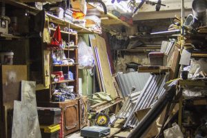 Überfüllte Werkstatt mit verschiedenen Werkzeugen, Holzregalen voller Gegenstände und verstreuten Objekten wie Leitern und einem Staubsauger auf dem Dachboden.